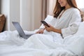 A beautiful young asian woman using mobile phone and laptop computer while lying down on bed Royalty Free Stock Photo