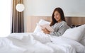 A beautiful young woman reading book in a white cozy bed at home Royalty Free Stock Photo