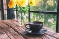 A black cup of hot coffee and yellow roses in a vase on vintage wooden table Royalty Free Stock Photo