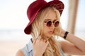 Closeup portrait of a blonde girl with round floral sunglasses,curly hair and hat, looking at the side. Royalty Free Stock Photo