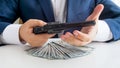 Closeup photo of businessman holding revolver and looking at big stack of money