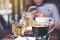 Closeup image of cups of hot coffee and tea on vintage wooden table in cafe with blur woman using smart phone Royalty Free Stock Photo