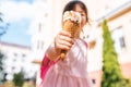 Closeup image of cute little girl walking along city street and eating ice cream outdoor. Happy kid girl showing her ice-cream in Royalty Free Stock Photo