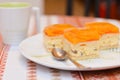 Closeup image of delicious slice of apricot cake lays on a white plate with a cup of cocoa on the table