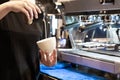 Closeup image of female barista pouring milk and preparing fresh cappuccino while standing in front of the coffee machine at Royalty Free Stock Photo