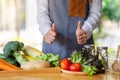 A female chef making and showing thumbs up hand sign while preparing fresh mixed vegetables to cook in kitchen Royalty Free Stock Photo