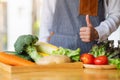 A female chef making and showing thumbs up hand sign while preparing fresh mixed vegetables to cook in kitchen Royalty Free Stock Photo