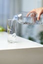 Closeup image of a female hand holding drinking water bottle and pouring water into glass on table. Royalty Free Stock Photo