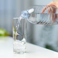 Closeup image of a female hand holding drinking water bottle and pouring water into glass on table on kitchen. Royalty Free Stock Photo