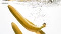 Closeup photo of fresh ripe yellow bananas falling and splashing in clear water against isolated white backgorund Royalty Free Stock Photo