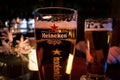 Closeup image of a glass of beer with the Heineken brand sign illuminated.