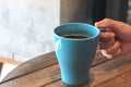 A hand holding blue mug of hot coffee on vintage wooden table in cafe Royalty Free Stock Photo