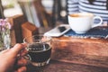 Closeup image of a hand holding cup of hot black coffee and tea on vintage wooden table in cafe with blur woman and smart phone Royalty Free Stock Photo