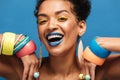 Closeup image of happy mulatto woman with colorful makeup laughing and showing beautiful adornment on her arms, isolated over blue