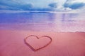 Closeup image of heart symbol written on sand at pink sunrise