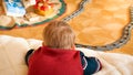 Closeup photo of little boy lying on floor and looking at his toy train riding on railways at living room Royalty Free Stock Photo