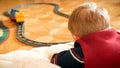 Closeup photo of little boy watching his toy train riding on railways on wooden floor at house Royalty Free Stock Photo