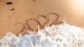 Closeup photo of ocean wave rolling over 2022 New Year numbers written on wet sand at island beach. Concept of New Year Royalty Free Stock Photo