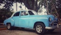 Closeup image of old blue car under green tree at Cuban resort