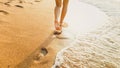 Closeup image of sexy barefoot female feet walking on the wet sand and calm warm waves at sea beach