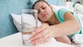 Closeup image of sick woman lying in bed and holding glass of water Royalty Free Stock Photo