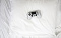 Closeup image top view game controller, lying on white sheets of bed at home with copy space