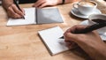 Two business man writing down on a white blank notebook with coffee cup on wooden table in office Royalty Free Stock Photo