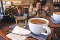 Two white cups of hot coffee and a glass of tea on vintage wooden table with a woman using mobile phone in cafe Royalty Free Stock Photo