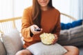 A woman eating pop corn and searching channel with remote control to watch tv while sitting on sofa at home Royalty Free Stock Photo