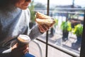 A woman holding and eating whole wheat sandwich and coffee in the morning