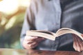 A woman holding and reading a vintage novel book on wooden table