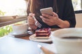 Closeup image of a woman holding , using and looking at smart phone while eating a cake with white coffee cups Royalty Free Stock Photo