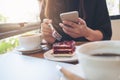 Closeup image of a woman holding , using and looking at smart phone while eating a cake with white coffee cups and laptop Royalty Free Stock Photo