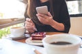 Closeup image of a woman holding , using and looking at smart phone while eating a cake with white coffee cups and laptop Royalty Free Stock Photo