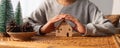 A woman protecting and covering wooden house model by hands with warmness