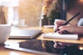 Closeup image of woman`s hand writing on a blank notebook with laptop , tablet and coffee cup on wooden table Royalty Free Stock Photo