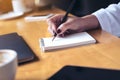 Woman`s hand writing on a blank notebook with laptop , tablet and coffee cup on wooden table background Royalty Free Stock Photo