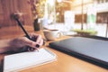 Closeup image of woman`s hand writing on a blank notebook with laptop , tablet and coffee cup on wooden table