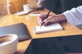 Closeup image of woman`s hand writing on a blank notebook with laptop , tablet and coffee cup on wooden table Royalty Free Stock Photo