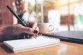 Closeup image of woman`s hand writing on a blank notebook with laptop , tablet and coffee cup on wooden table