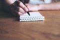 A woman`s hand writing down on a white blank notebook on wooden table