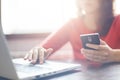 Closeup image of woman`s hands holding smartphone and typing something at keyboard of laptop. Young female searching information i Royalty Free Stock Photo