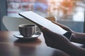 A woman`s hands holding and using tablet pc with coffee cup on wooden table with blur background in cafe