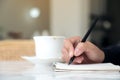 A woman`s hands writing down on a white blank notebook with coffee cup and dessert on table in cafe Royalty Free Stock Photo