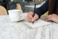 A woman`s hands writing down on a white blank notebook with coffee cup and dessert on table in cafe Royalty Free Stock Photo