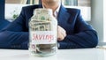 Closeup photo of young businessman looking at glass jar full of money Royalty Free Stock Photo