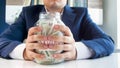 Closeup photo of young greedy businesman holding glass jar full of money in hands Royalty Free Stock Photo