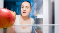 Closeup image of young hungry woman looking for something to eat in refrigerator at night Royalty Free Stock Photo