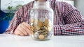 Closeup photo of young man sitting behind table with glass jar full of money Royalty Free Stock Photo