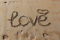 Closeup of Inscription of `Love`, a symbol of heart and footprints in the sand. Royalty Free Stock Photo